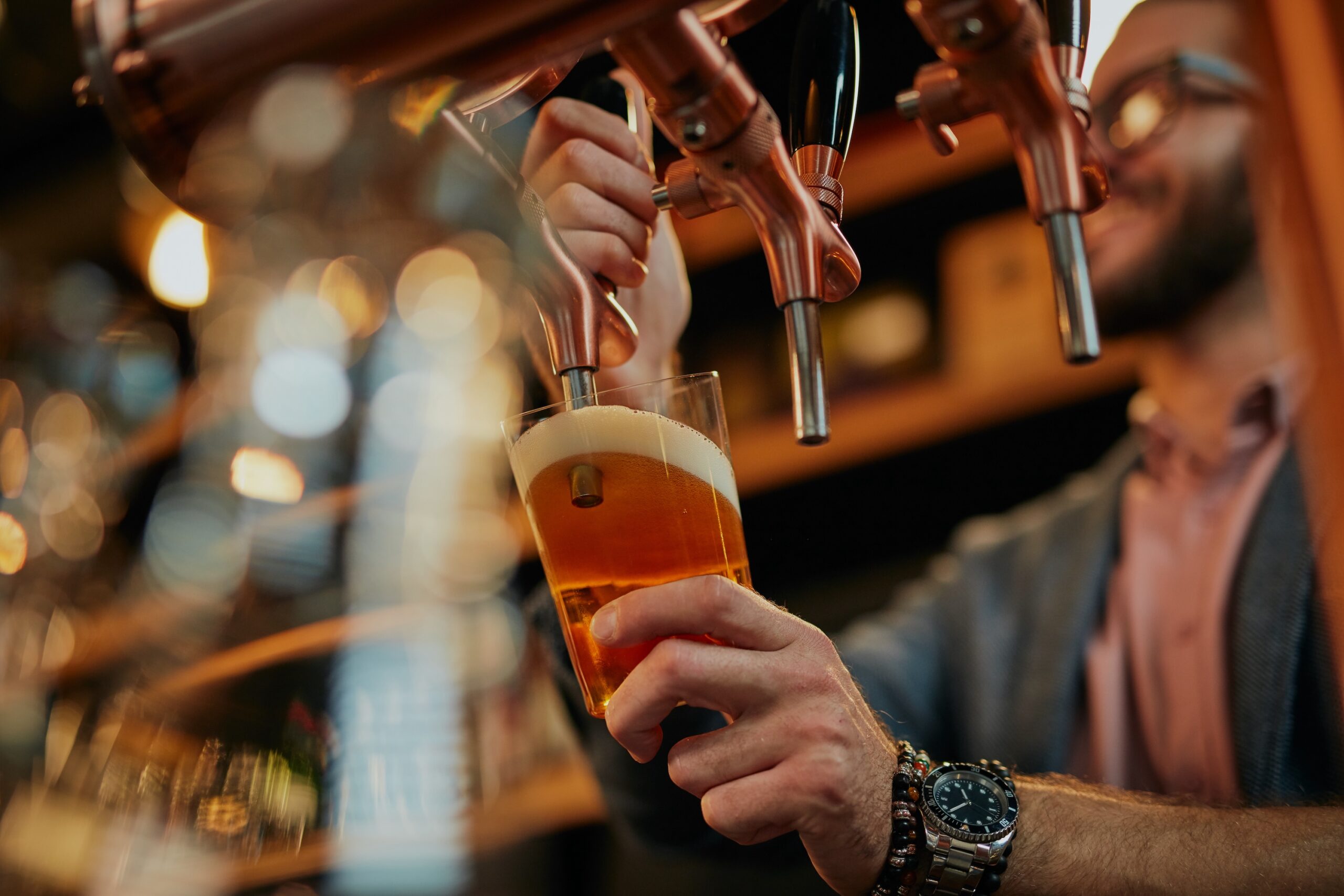 Bartender pouring a fresh draft beer from a copper tap into a glass in a dimly lit bar scaled