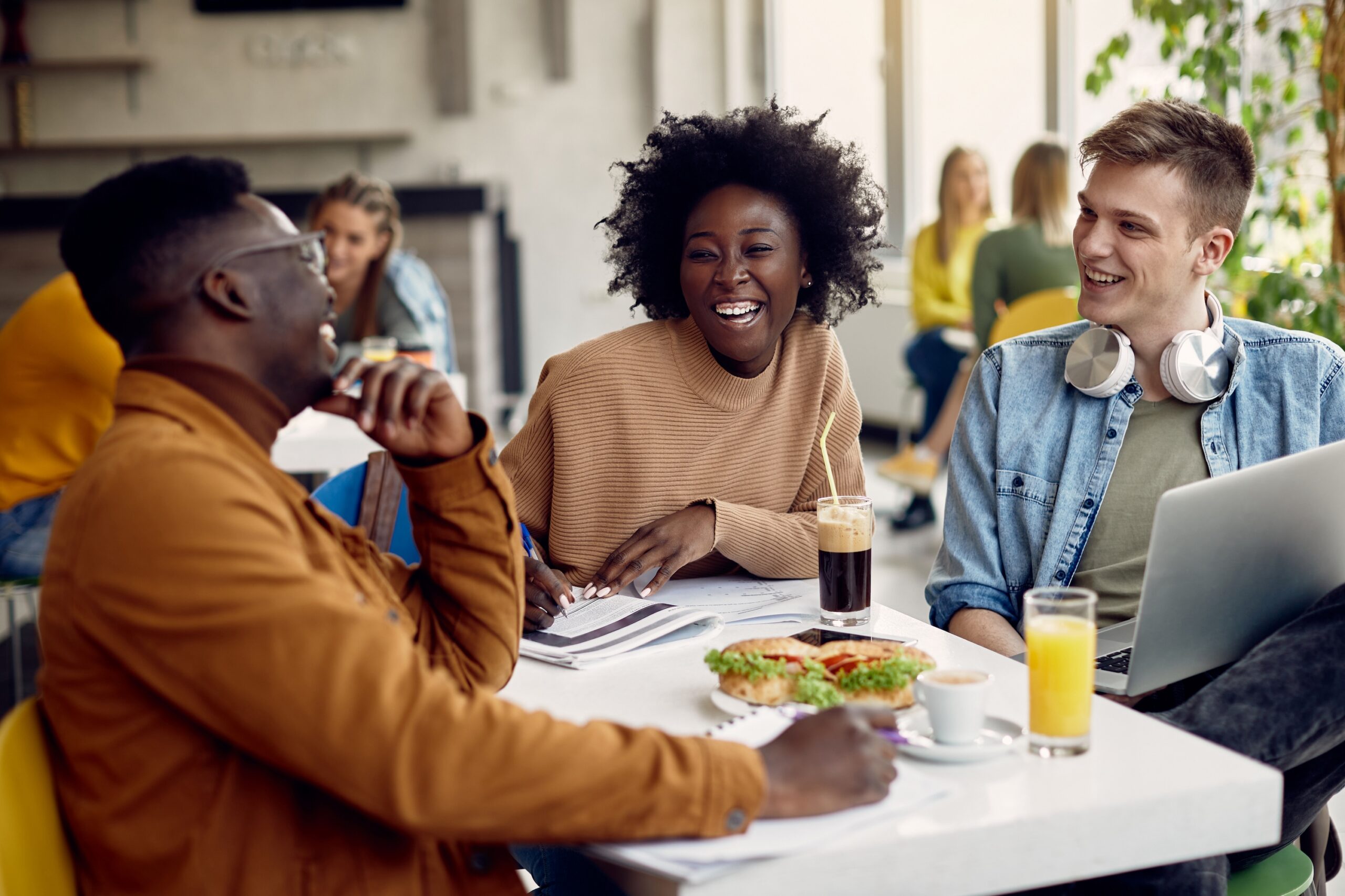 Diverse group of college students laughing together while studying at a cafe table with drinks and snacks scaled