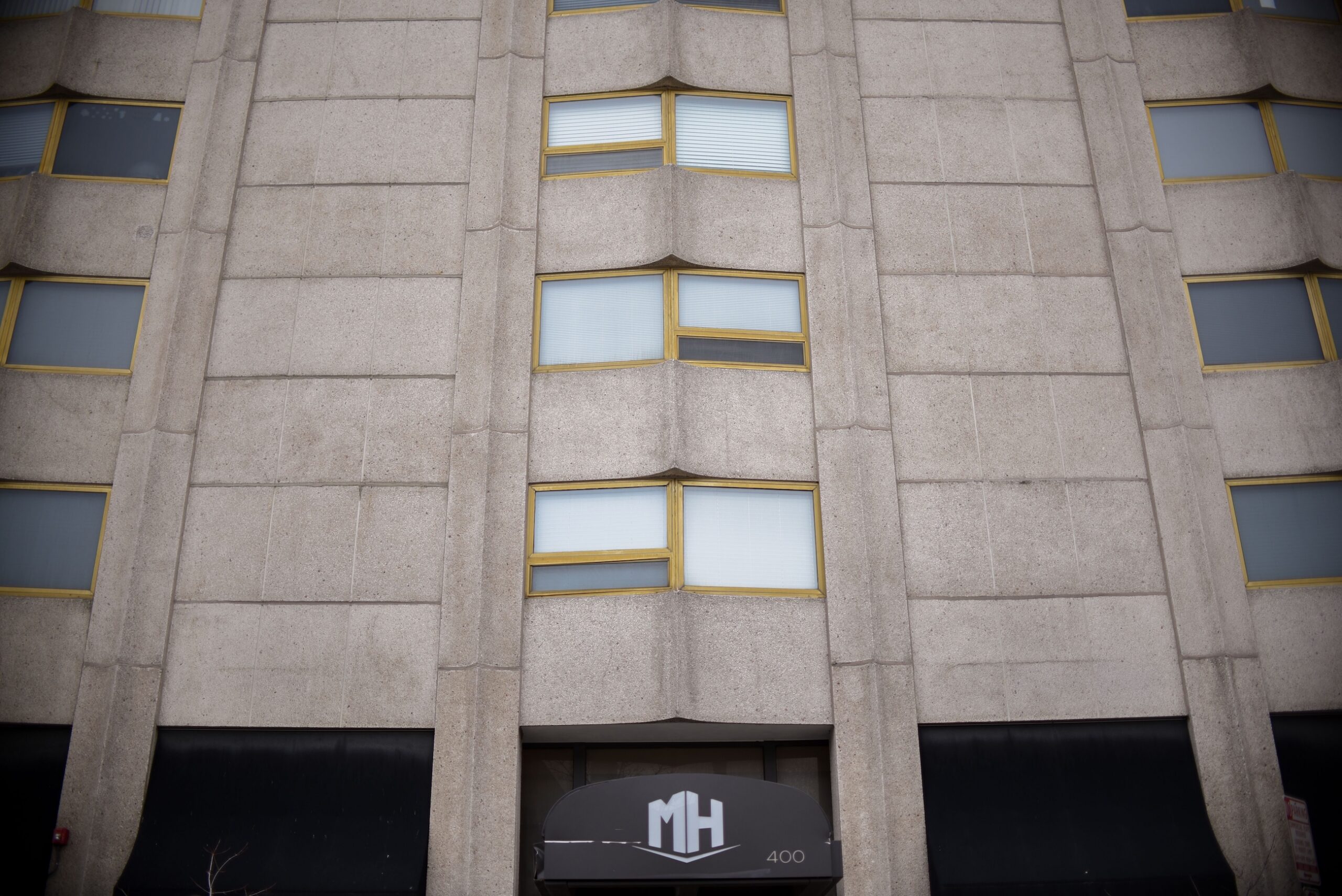 Exterior facade of multi story concrete apartment building with gold trimmed windows and entrance canopy scaled