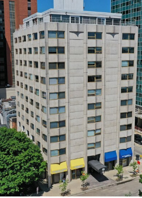 Exterior view of multi story concrete apartment building with street level retail awnings