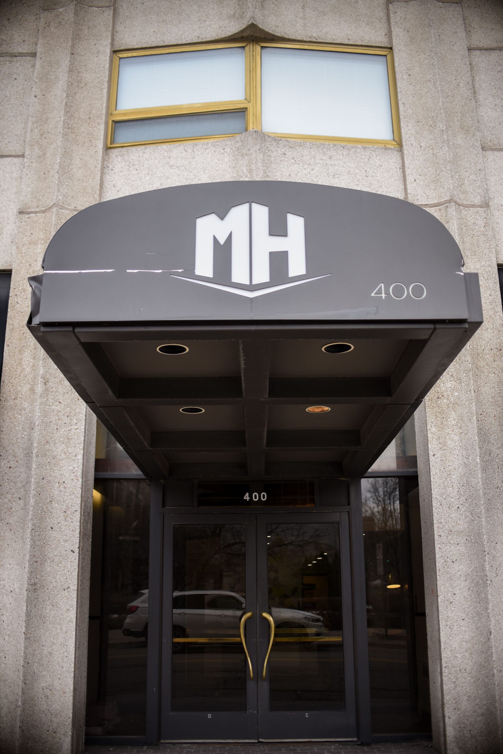 Main glass entrance doors of 400 building with black awning displaying MH logo scaled
