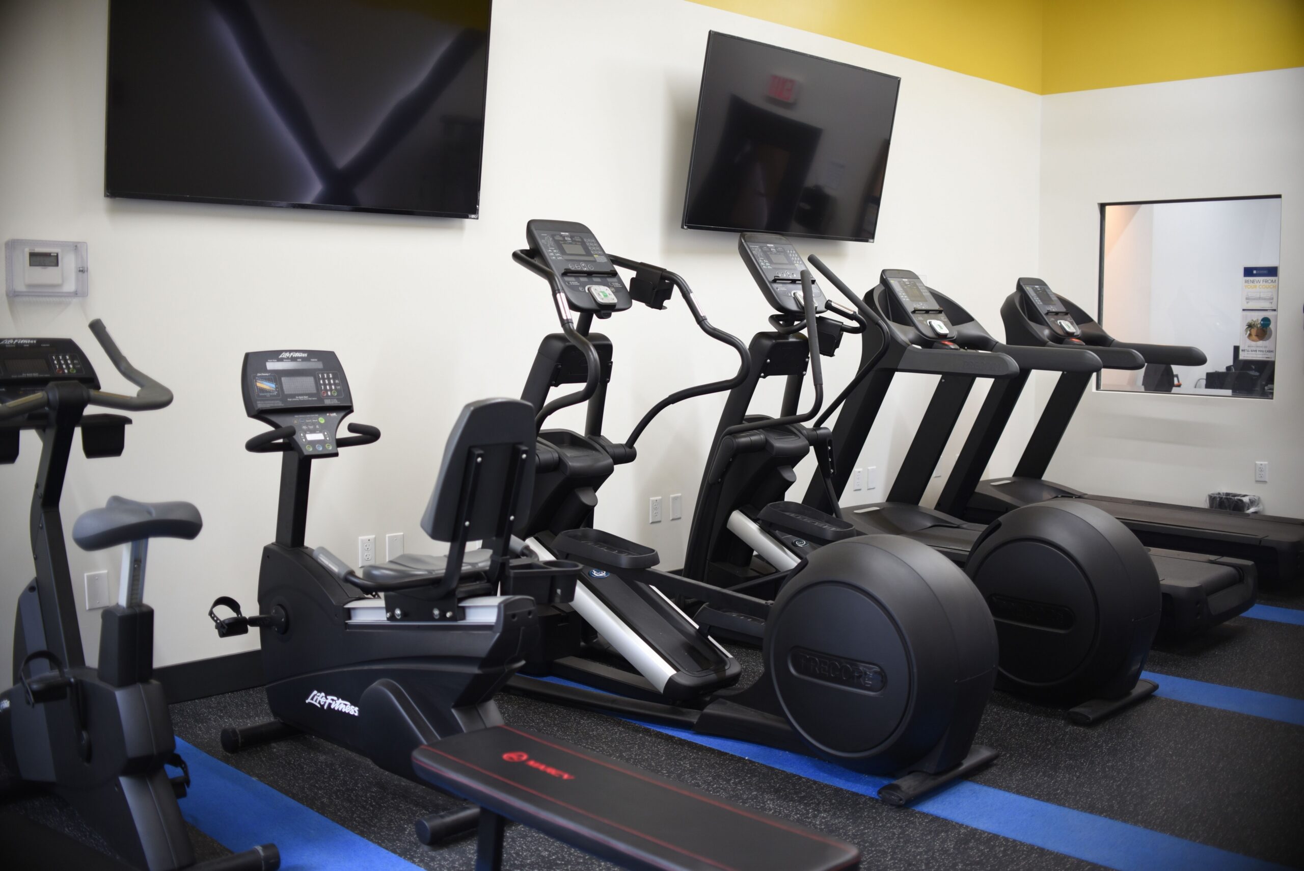 Modern apartment gym featuring cardio machines exercise bikes and wall mounted televisions scaled