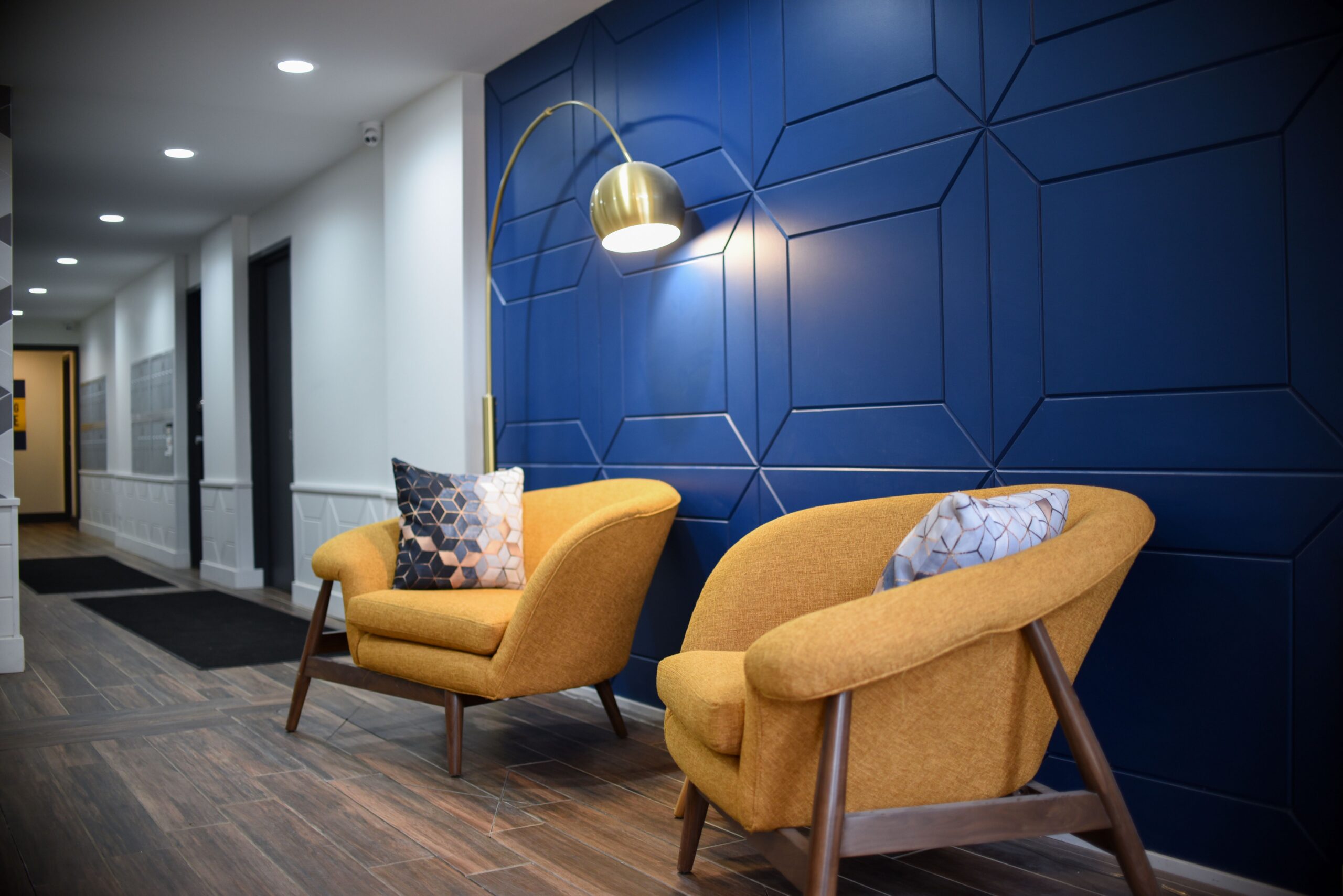 Stylish apartment lobby entrance featuring mid century yellow armchairs and decorative blue panel wall scaled